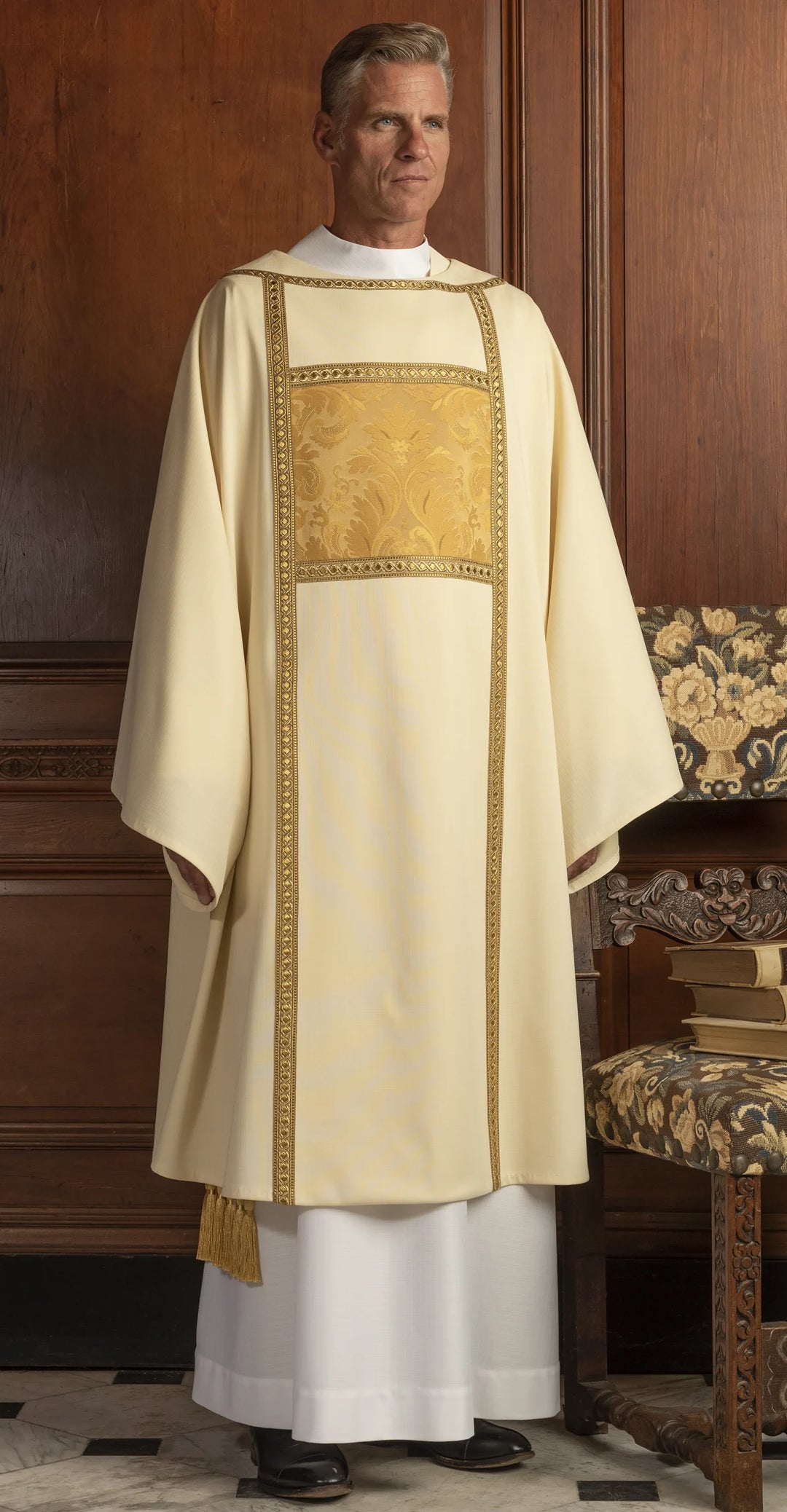 Man wearing a white and gold liturgical vestment in a room with wooden paneling.