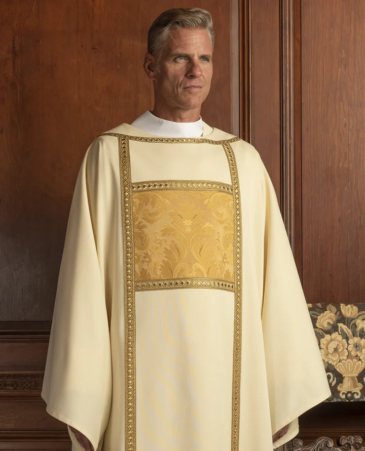 Man wearing a white liturgical vestment with gold embroidery against a wooden background