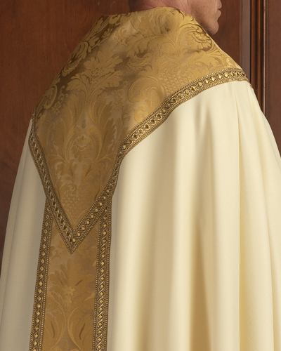 Close-up of a person wearing a white garment with gold embroidery against a wooden background