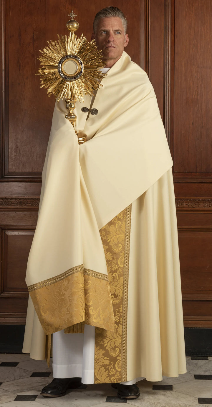 Person in religious attire holding a monstrance against a wooden panel background